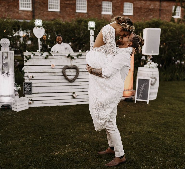 Groom picking up his bride in a lace wedding dress and dried flower crown at their outdoor evening reception with The Boombox UK DJ