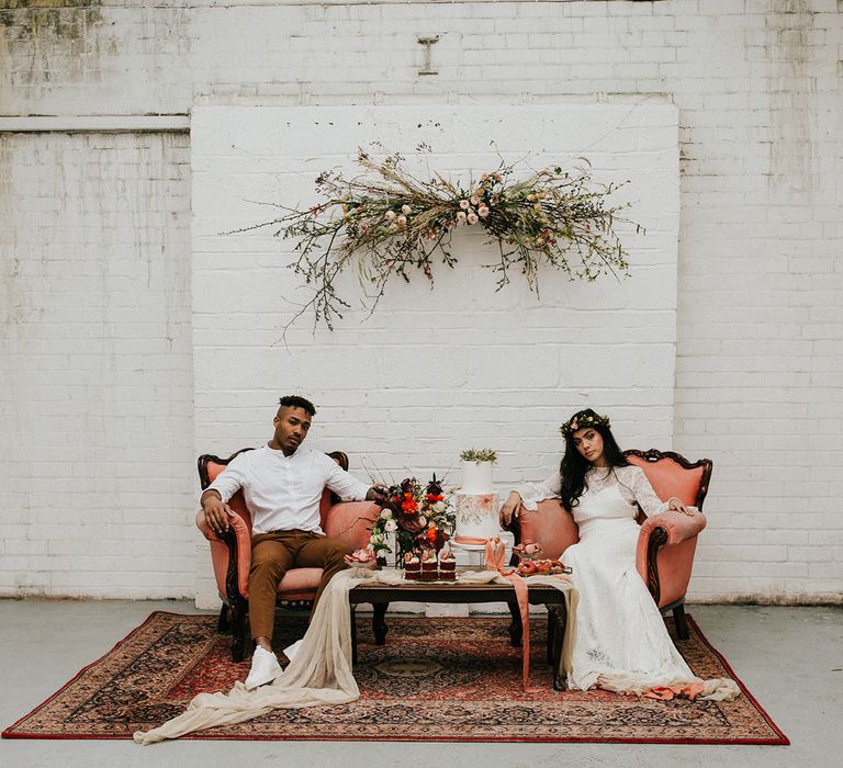 Chill out area in an industrial wedding venue with wool rug, ornate chairs and handing floral installation