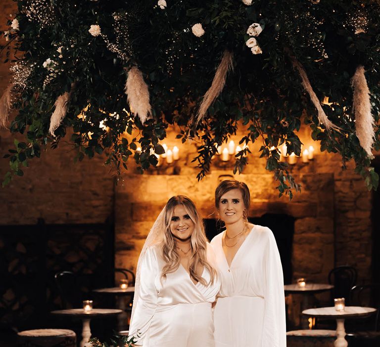 Brides stand with one another in rustic venue for post-wedding couples portraits