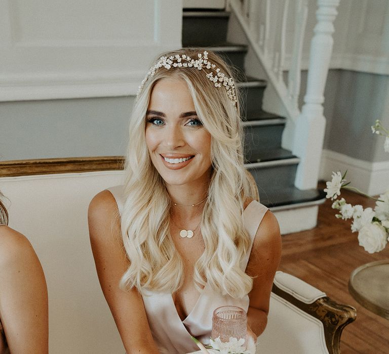 Beautiful bridesmaid with long wavy blonde hair and hair vine, wearing a champagne gold wrap bridesmaid dress, holding a white bouquet with anthuriums and roses