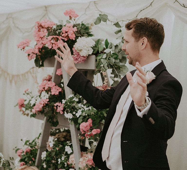 Grooms speech at the marquee back garden wedding reception with step ladder planter display in the background 