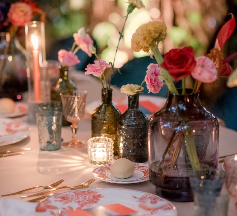 Colourful florals sit within different coloured vases next to patterned plates