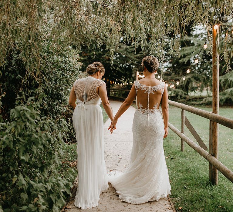 Brides hold hands outdoors as they walk down pathway on their wedding day