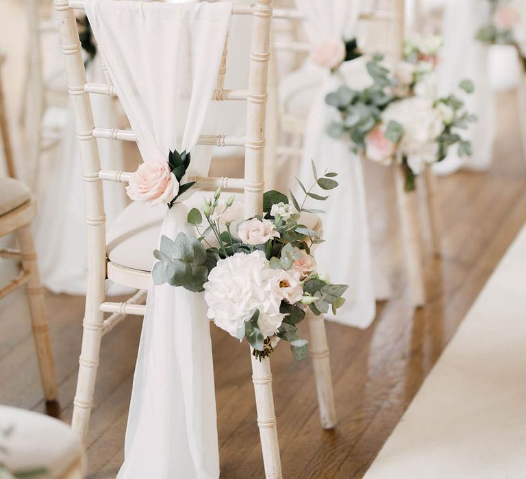 White wicker chairs complete with white fabric draped across and florals tied to the back