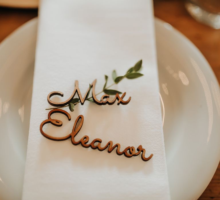 Wooden personalised table place names on white napkin with foliage stalk for rustic wedding decor 