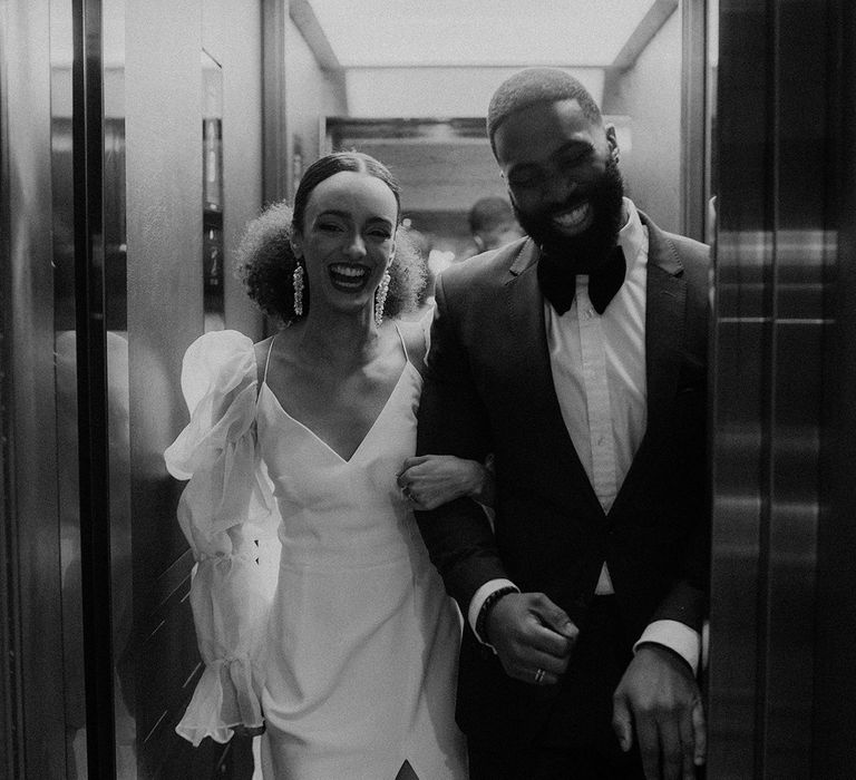 Black bride and groom in black-tie attire exiting the lift at Mayfair Townhouse wedding venue 