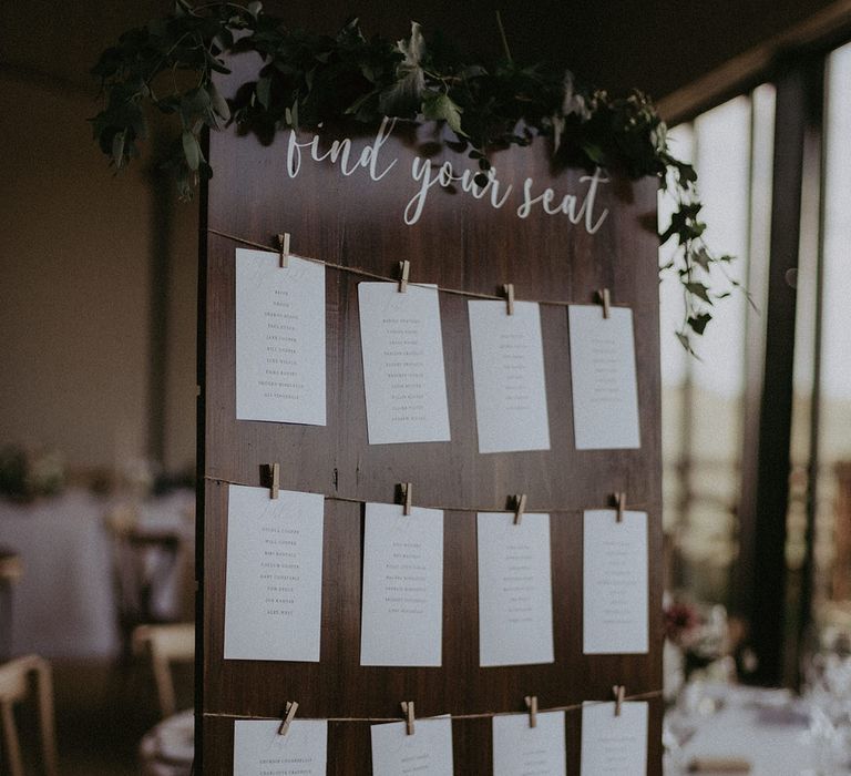 DIY seating chart on dark wooden board with pegs holding small white cards