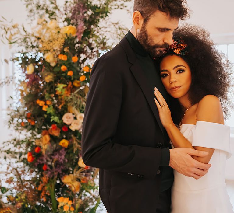 Black bride with afro hair in an off the shoulder wedding dress laying on her grooms chest in a black suit and top