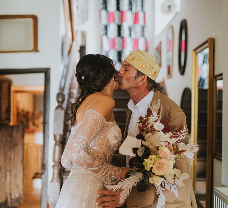 Father of the bride in yellow suit and matching hat kisses bride on her cheek in Zavana Couture wedding dress