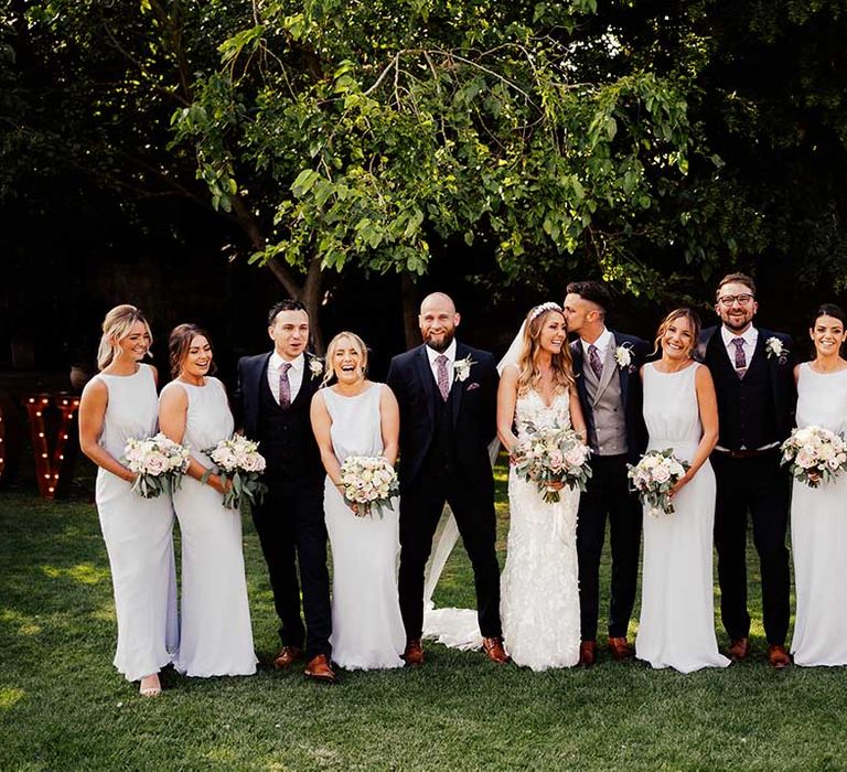 Wedding party with bridesmaids in grey high neck low back dresses with groomsmen in dark three piece suits and paisley ties with bride and groom