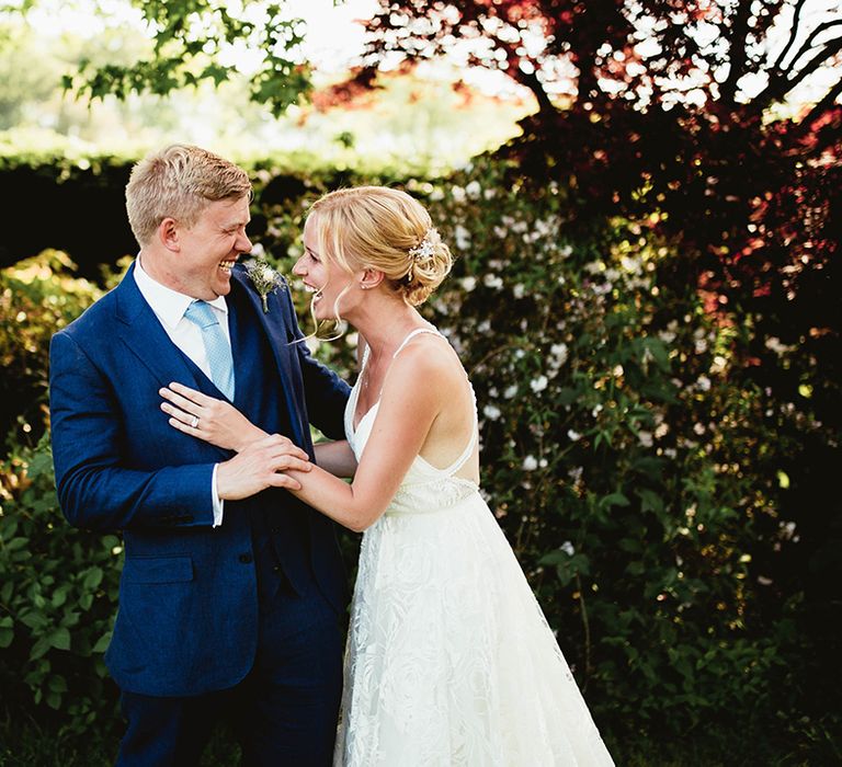 Laughing bride and groom in blue suit and boho lace wedding dress share joy together 