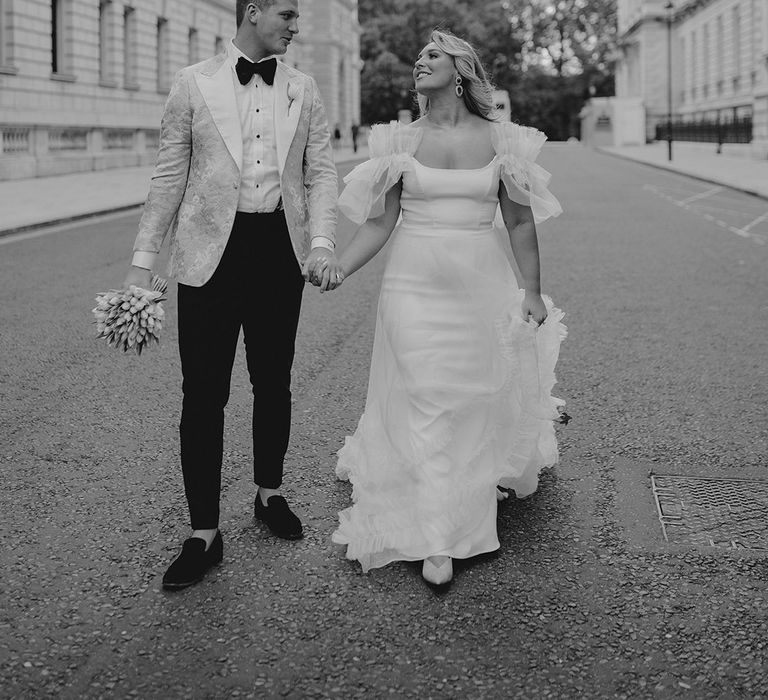 Bride and groom walk around London together with bride in Halfpenny London dress and groom in black tie with custom gold tuxedo