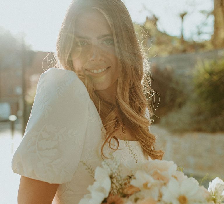 Bride in puff sleeve patterned wedding dress holding pink and white wedding bouquet with roses, cosmos and daisies 