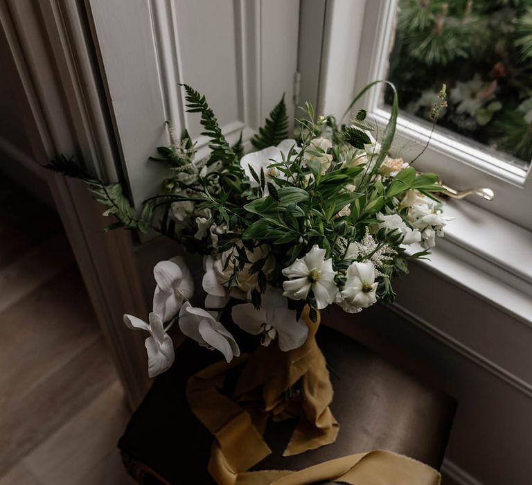 White and green wedding bouquet tied with ribbon resting on a window ledge 