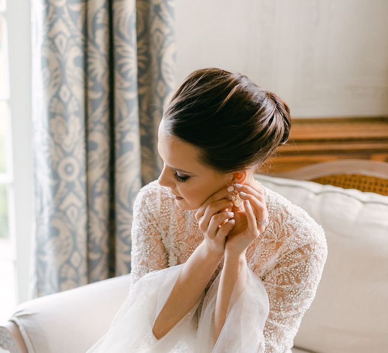 Bride with a chic bun and embellished wedding dress putting on her wedding earrings 