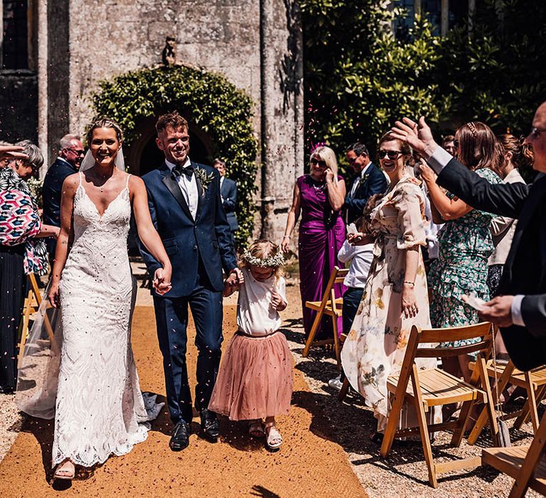 Bride and groom walk with their daughter through confetti as they have confetti exit from outdoor wedding ceremony 