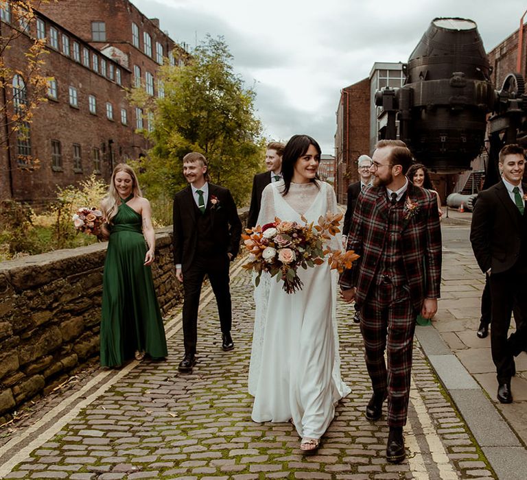 Bride & groom walk with their groomsmen and bridesmaids as bridesmaids wear green gowns complete with crossover waistband