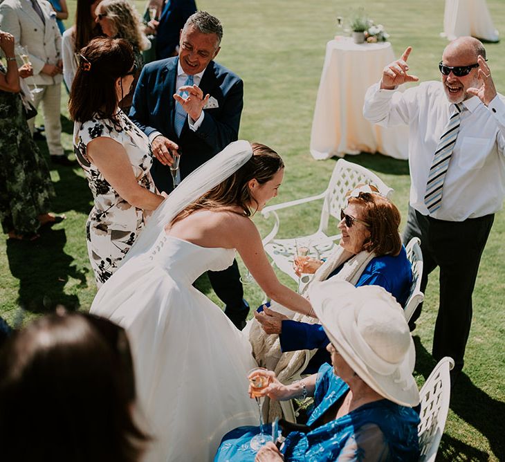 Bride greets wedding guests outdoors in Cowdray House gardens 