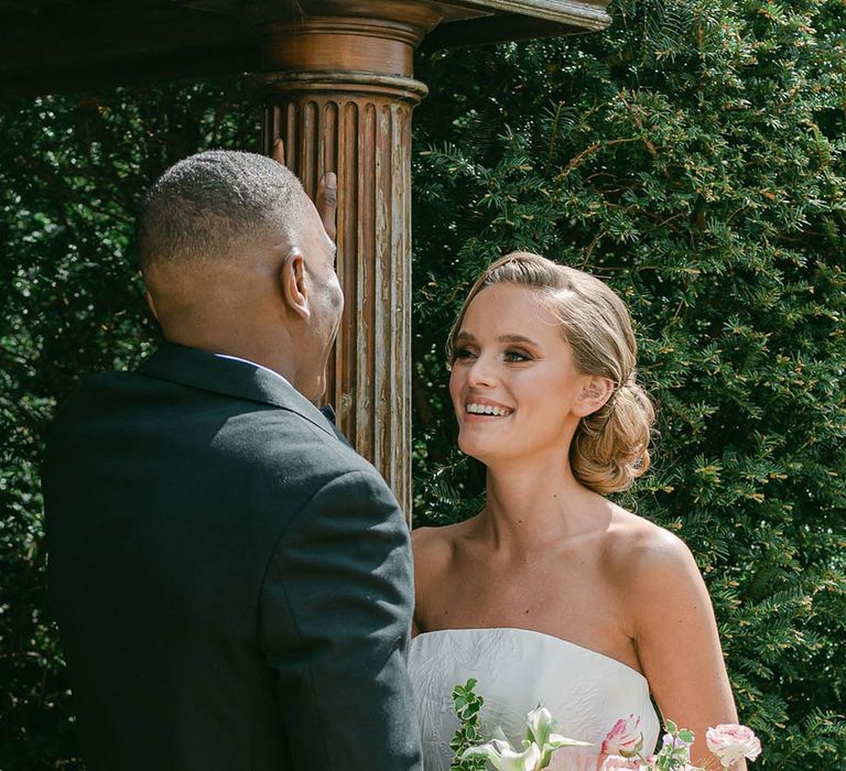 Bride in strapless Jesus Peiro wedding dress with a pastel wedding bouquet smiling at the groom 