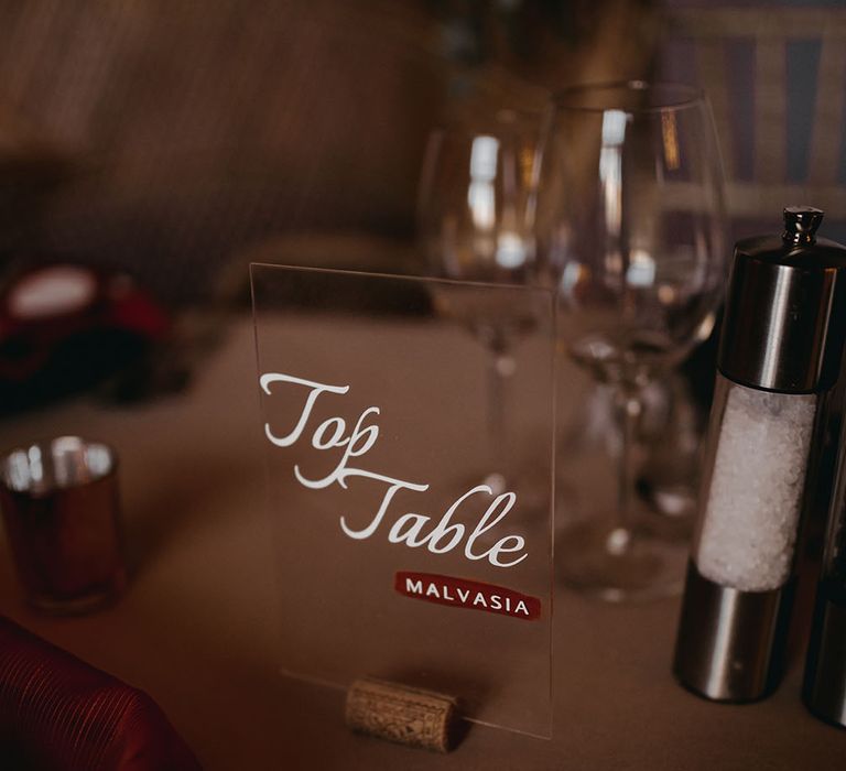 Top table written in white writing on clear perspex glass with wine cork to the bottom 