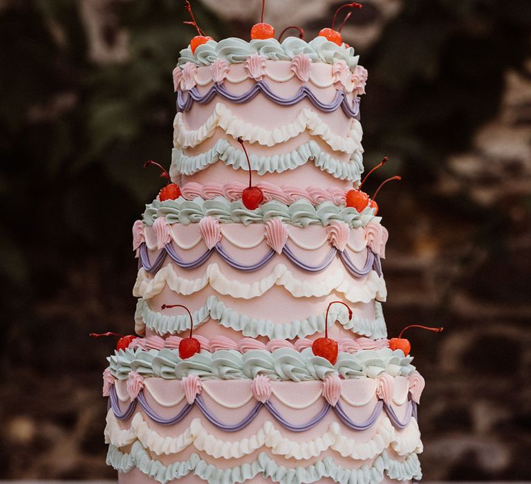 Three tier pastel colour retro iced wedding cake with purple, pink, green and and white icing with cherries 