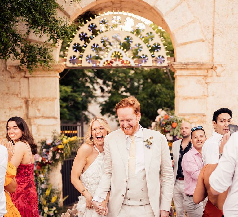 Bride and groom enter their outdoor wedding reception with the wedding guests applauding on their feet