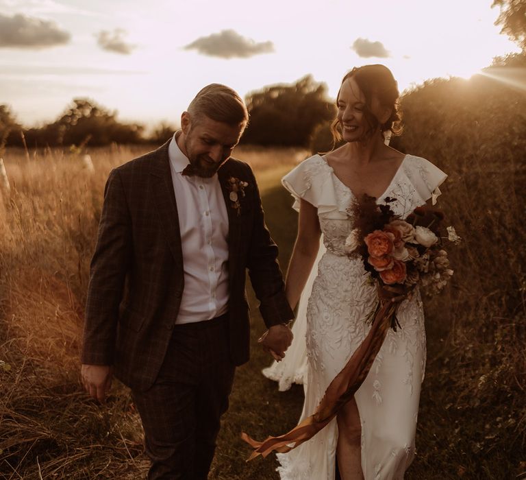 Bride and groom walk hand in hand during sunset got their rustic luxe barn wedding