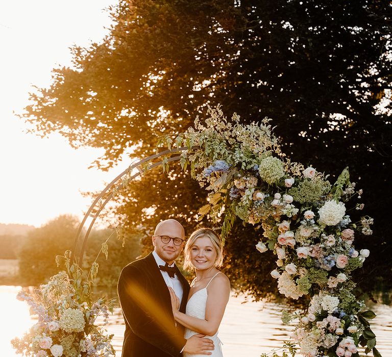 Bride & groom stand beneath steel floral archway during golden hour