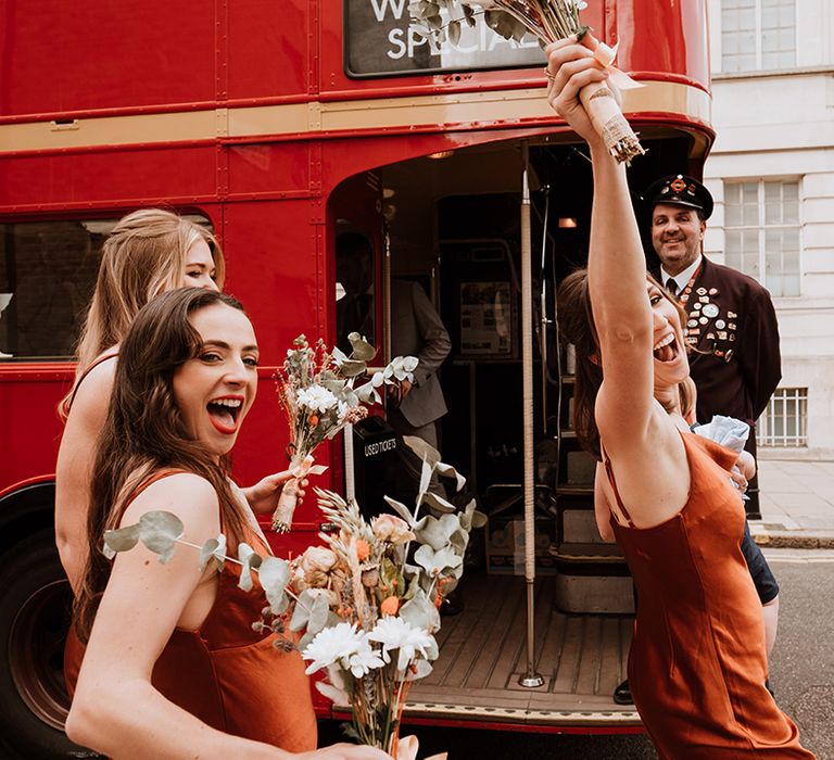 Bridesmaids in different styled burnt orange bridesmaid dresses carry dried floral bouquets 