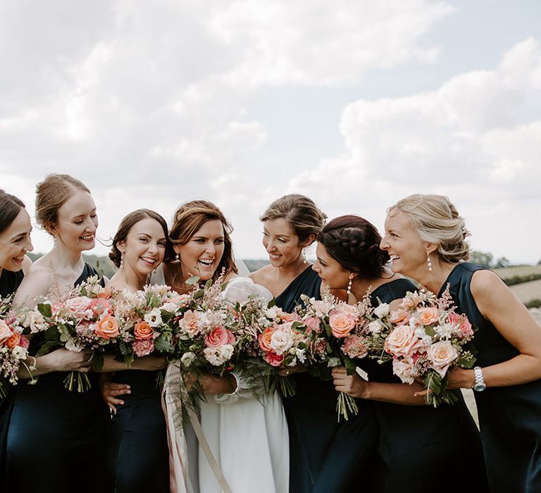 Bride stands with her bridesmaids in deep blue satin bridesmaid dresses whilst holding colourful floral bouquets 