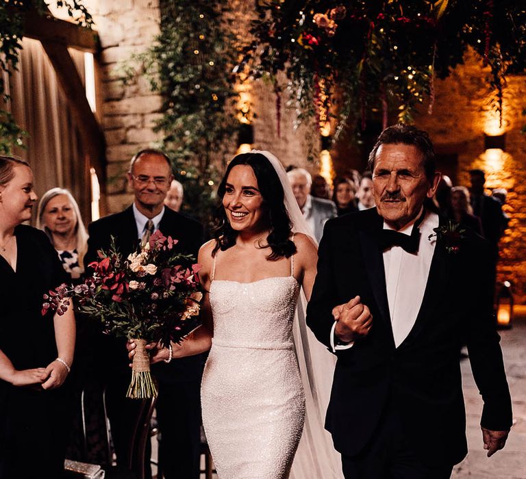 Father of the bride in black tie walks the bride down the aisle in a sparkly wedding dress and pink bouquet of flowers 