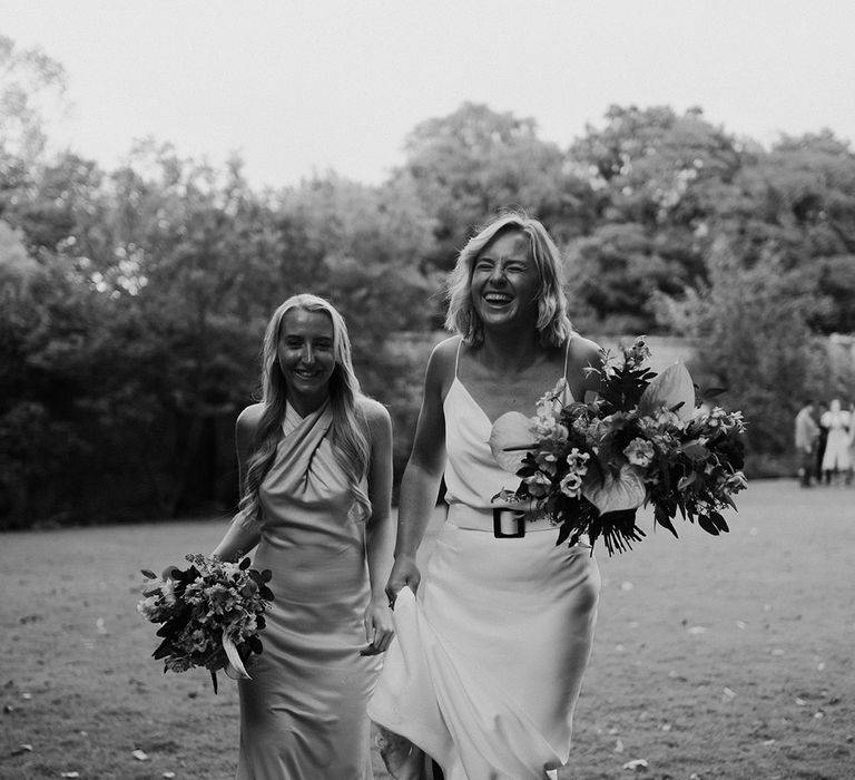 Bride walks with bridesmaid wearing halter-neck styled satin bridesmaid dress 