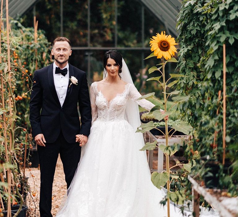 The bride and groom pose with a tall sunflower at Elmore Court 