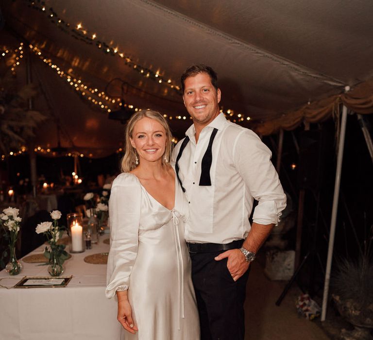 Bride in second white dress for the evening posing and smiling with the groom in a white shirt and undone bow tie 