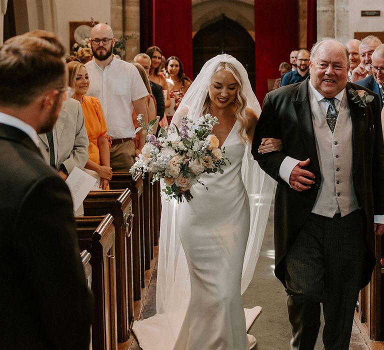 Father of the bride in a three piece suit walks down the aisle with the bride to meet the groom at the altar 