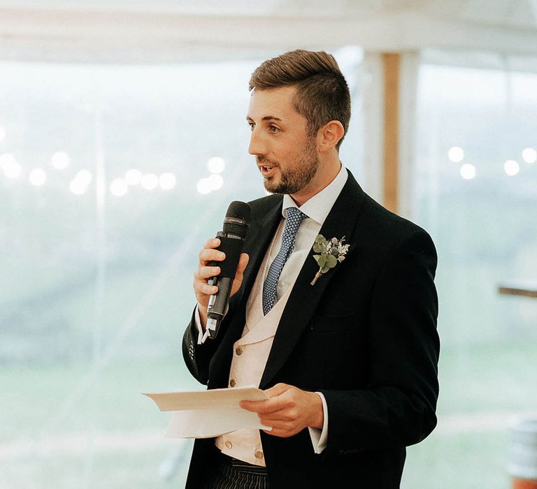 Groom wears morning suit and floral buttonhole as he gives speech during reception