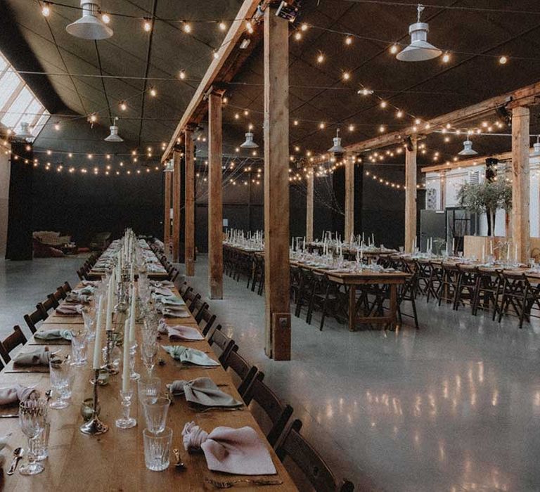 Wooden banquet tables in industrial setting complete with festoon lighting 