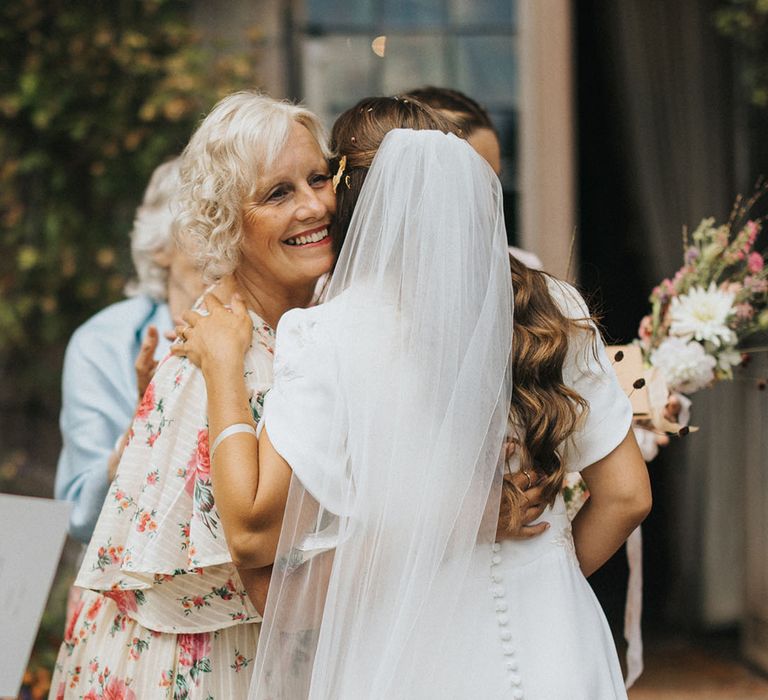 Bride in handmade wedding dress with button back detail hugging a wedding guest giving their congratulations for Askham Hall wedding 