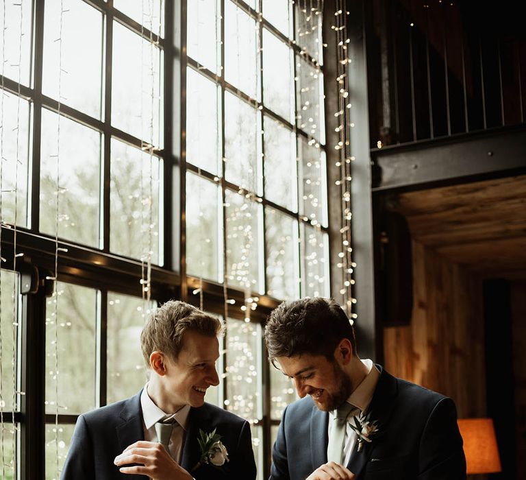 The groom gets ready with a groomsman wearing matching navy blue su8it and sage green ties for the rustic luxe wedding at Hidden River Cabins