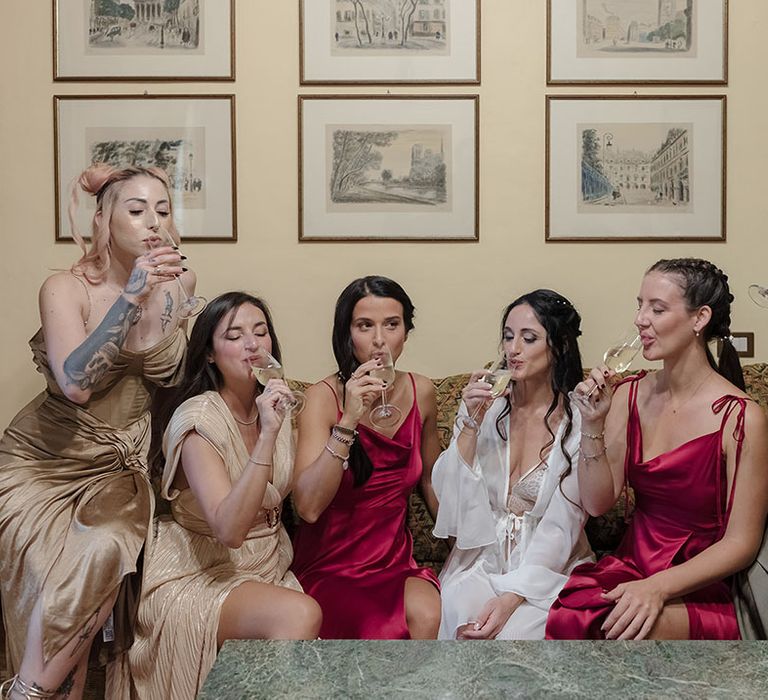 Bride sips champagne with her bridal party and bridesmaids in satin burgundy bridesmaid dresses 