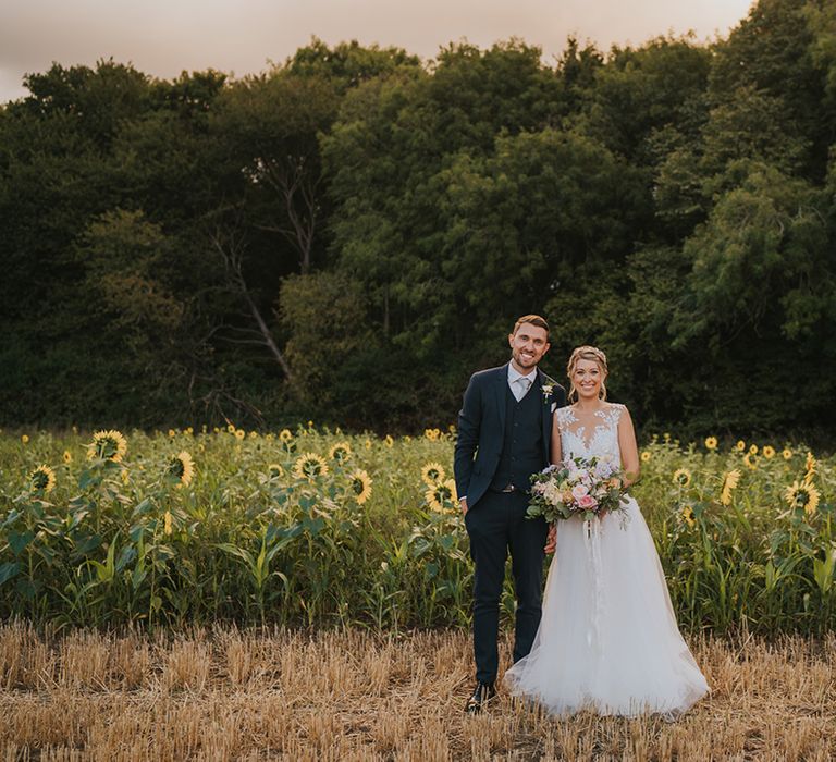 The bride and groom smile together for their couple portraits in a sunflower field 