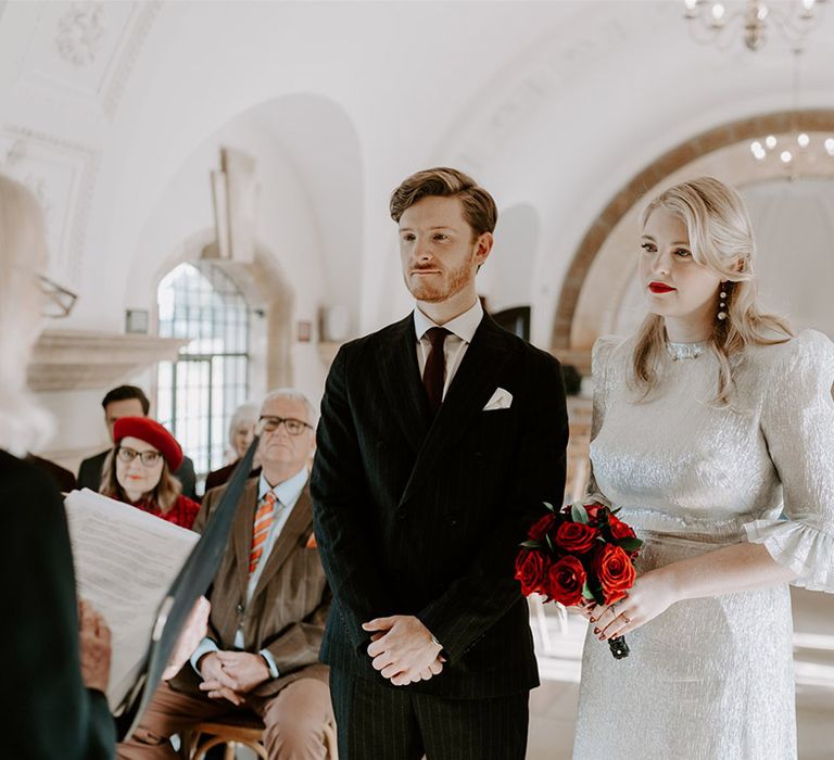 Elopement style wedding planned in six months with the bride holding a small round red rose bouquet with red lipstick 