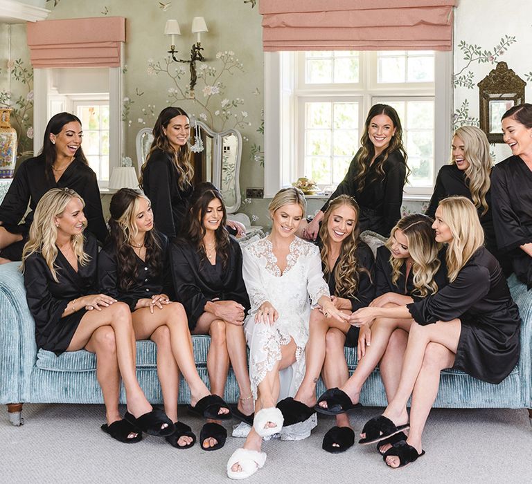 Bridesmaids in matching black satin bridesmaid robes and slippers with the bride as they get ready for the wedding 