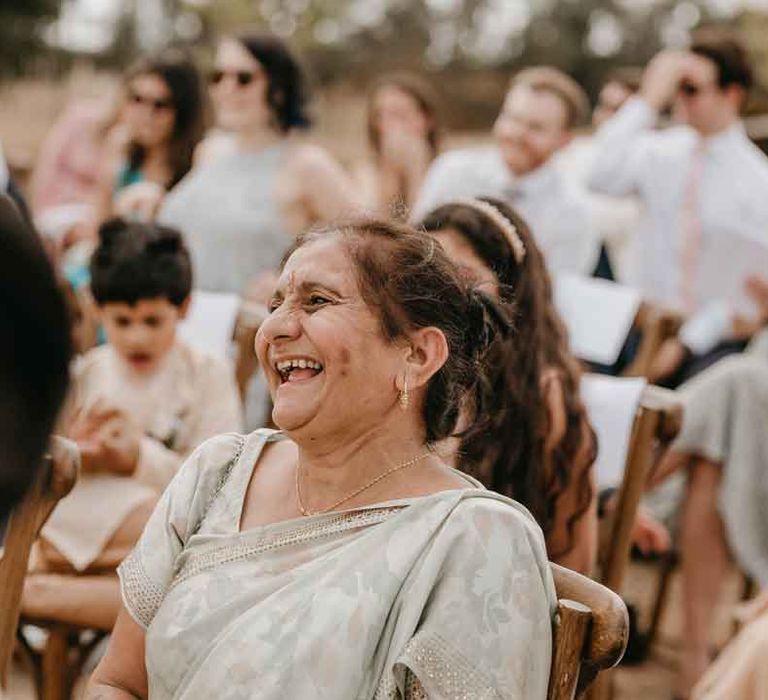 Wedding guest in sage green Indian lehenga laughing at wedding speeches at High Billinghurst Farm Gujarati wedding ceremony 