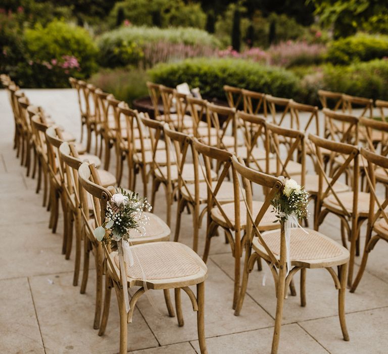 Outdoor seating area for summer wedding with the chairs decorated with pale pink rose chair back decor