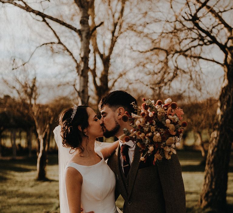 Rustic luxe wedding in spring with the bride and groom sharing a kiss with rustic dried wedding flower bouquet 