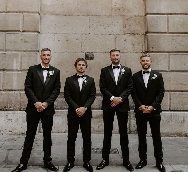 Groomsmen pose together in their matching black tuxedos and white flower buttonholes 