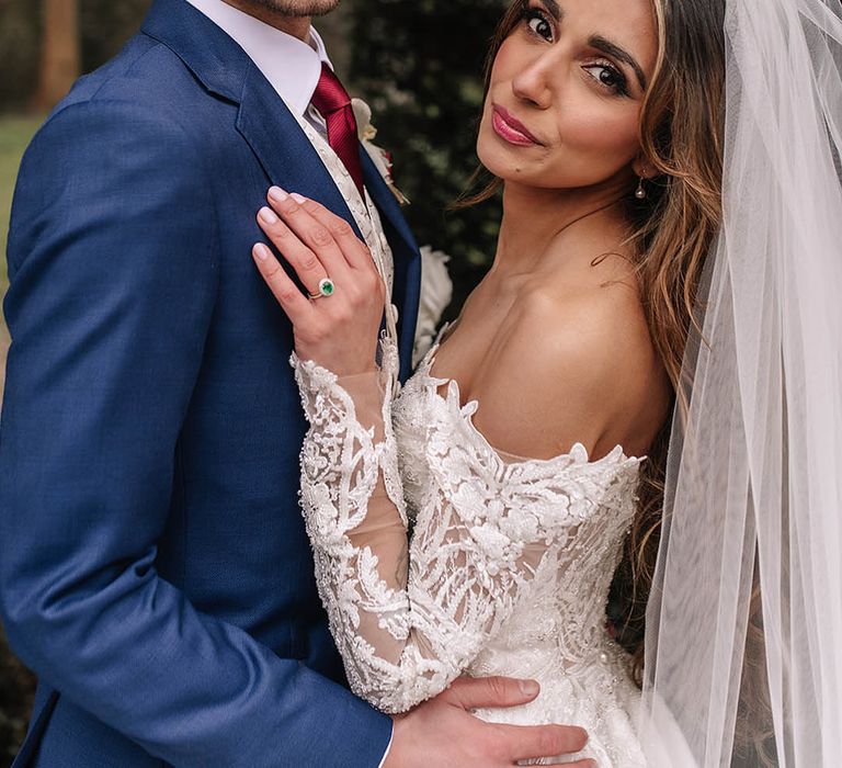 Groom in blue suit posing with bride in sequin wedding dress for couple portraits with emerald engagement ring 