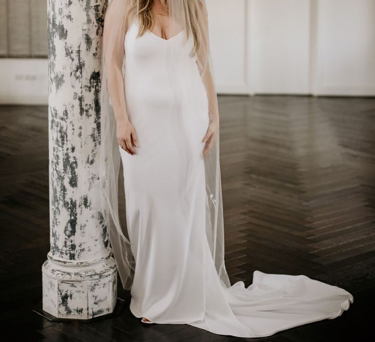 Bride in simple satin wedding dress with plunging neckline paired with long wedding veil 