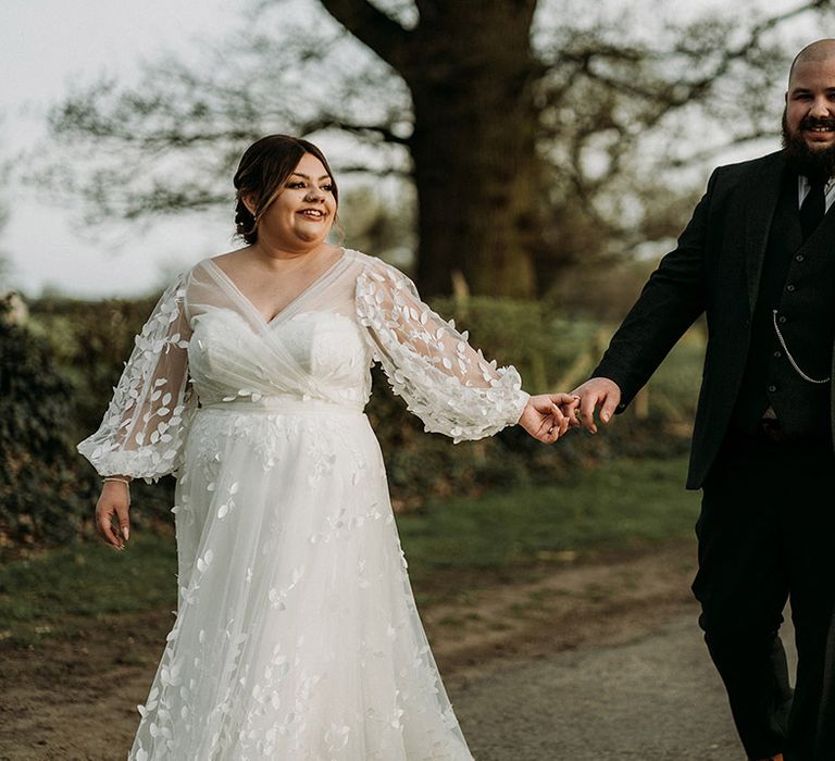 Groom in three piece green tweed wedding suit walking hand in hand with the bride in a long sleeve wedding dress 